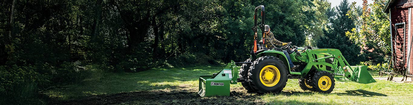 A man using a John Deere 3E Compact Tractor with a Frontier box blade to grade the ground.