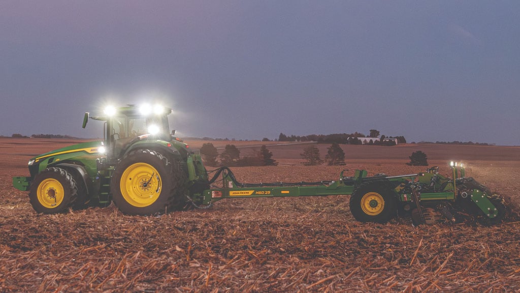 Un John Deere 8R 410 tirant un pulvériseur à disques à grande vitesse HSD25 dans un champ la nuit