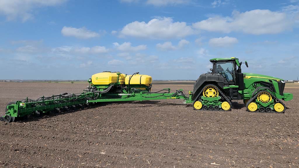 Un tracteur vert dans un champ, sous un ciel bleu.