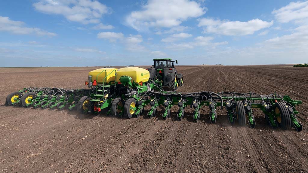 Un John Deere 8RX 410 tirant un semoir tracté 1775NT dans un champ.