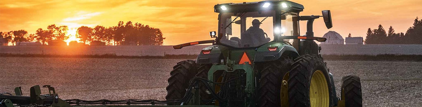 Un tracteur John Deere de la série&nbsp;8 pour cultures en lignes dans un champ au coucher du soleil.