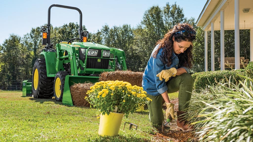 femme travaillant dans un parterre de fleurs avec un tracteur de la série 3 en arrière-plan"