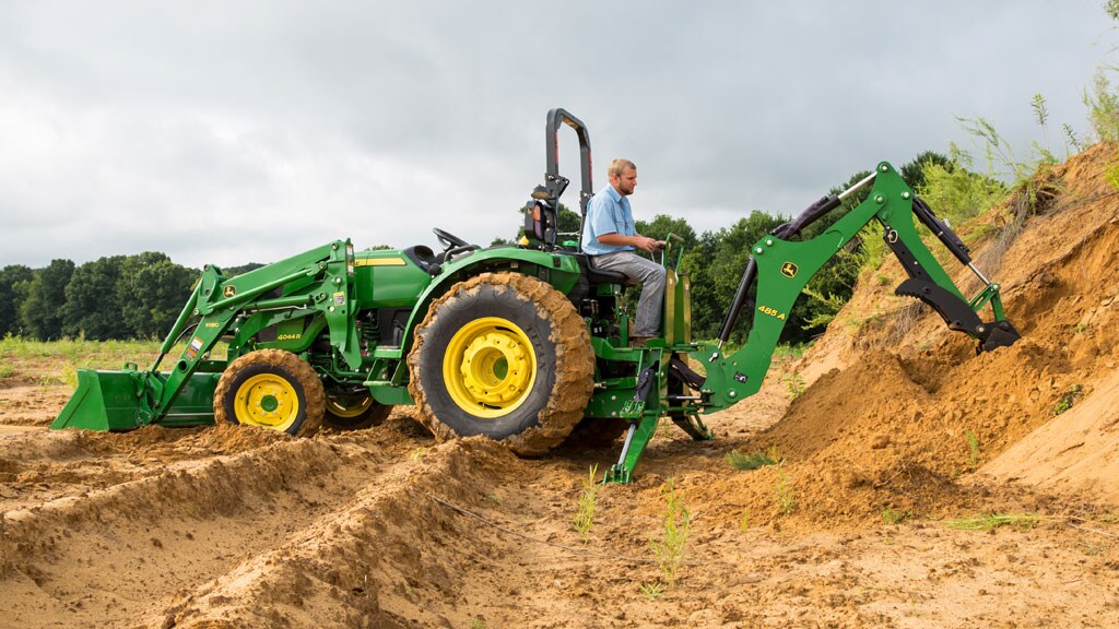 Un homme sur un tracteur avec chargeur et pelle rétro creuse dans le sol avec la pelle rétro