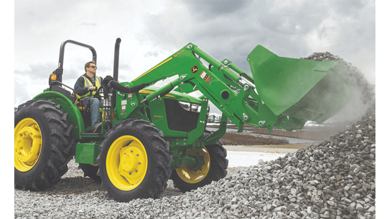 Une personne portant un gilet de sécurité utilise un chargeur frontal fixé à un tracteur vert pour prélever des cailloux dans un tas.