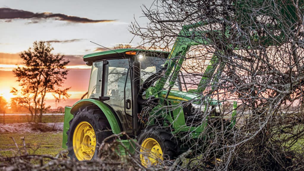 tracteur utilitaire 5e soulevant des branches d’arbre à l’aide d’un chargeur frontal