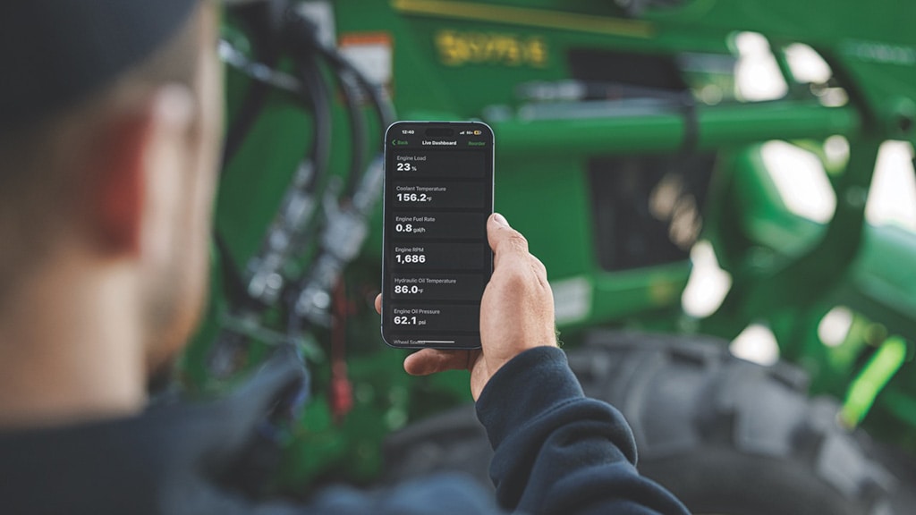 Une personne consulte sur son téléphone les indicateurs de l’équipement, comme la charge et le régime du moteur, par l’intermédiaire de JDLink.