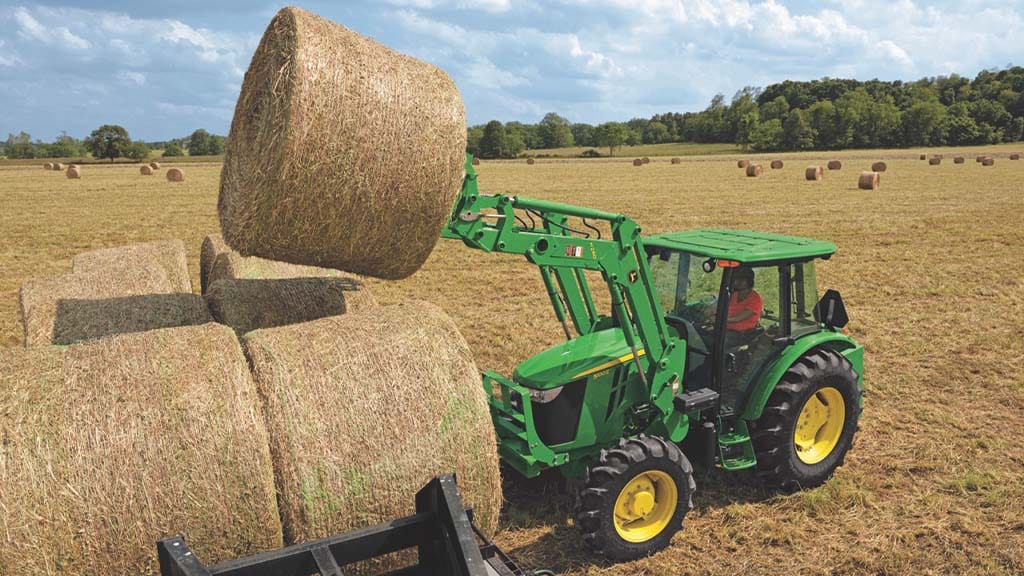 Un tracteur vert utilise une pointe à balles pour empiler des balles de foin dans un champ de foin fauché et mis en balles.