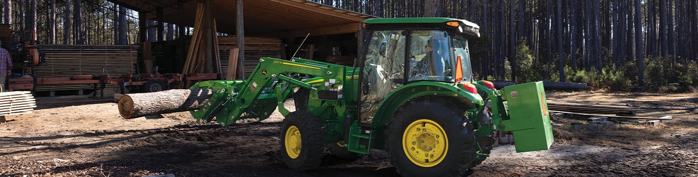 Un accessoire de grappin est utilis&eacute; par un tracteur vert pour d&eacute;placer des rondins sous un espace de rangement ouvert.