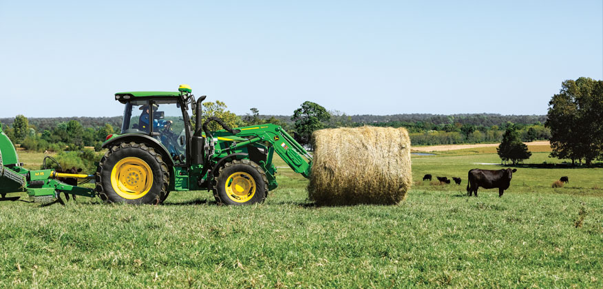 tracteur 5M déplaçant une balle de foin pour des vaches dans un pâturage