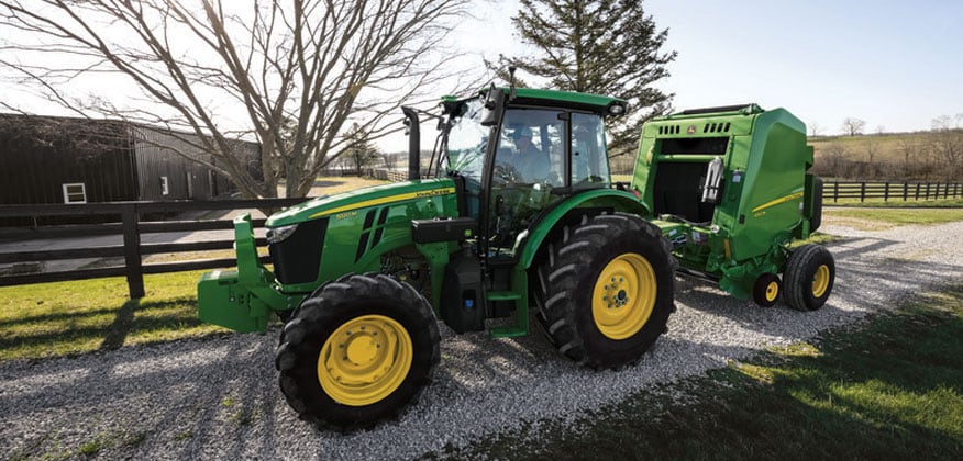 5M tractor driving down a gravel road next to a fence