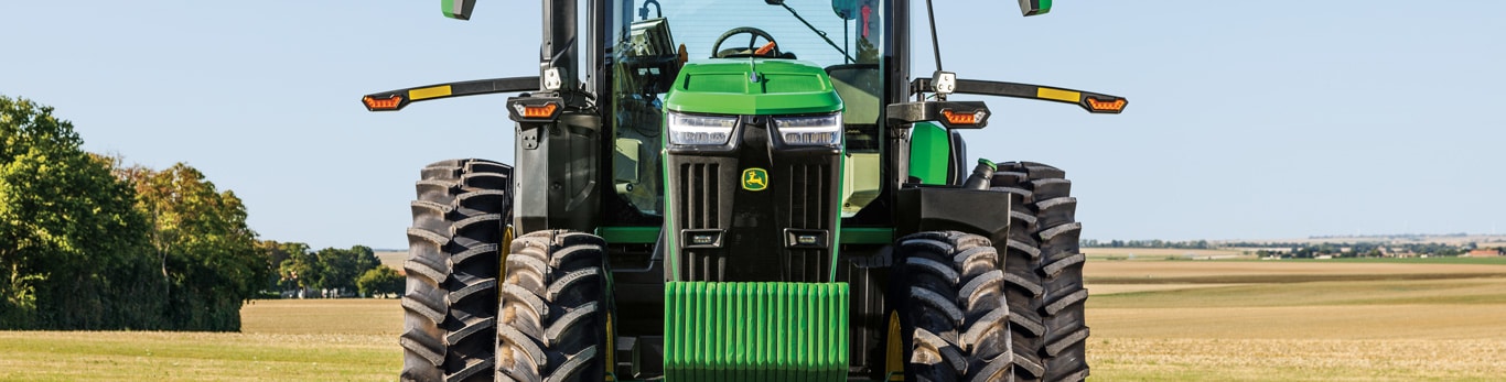 Front view of John Deere tractor in an open field under clear sky.