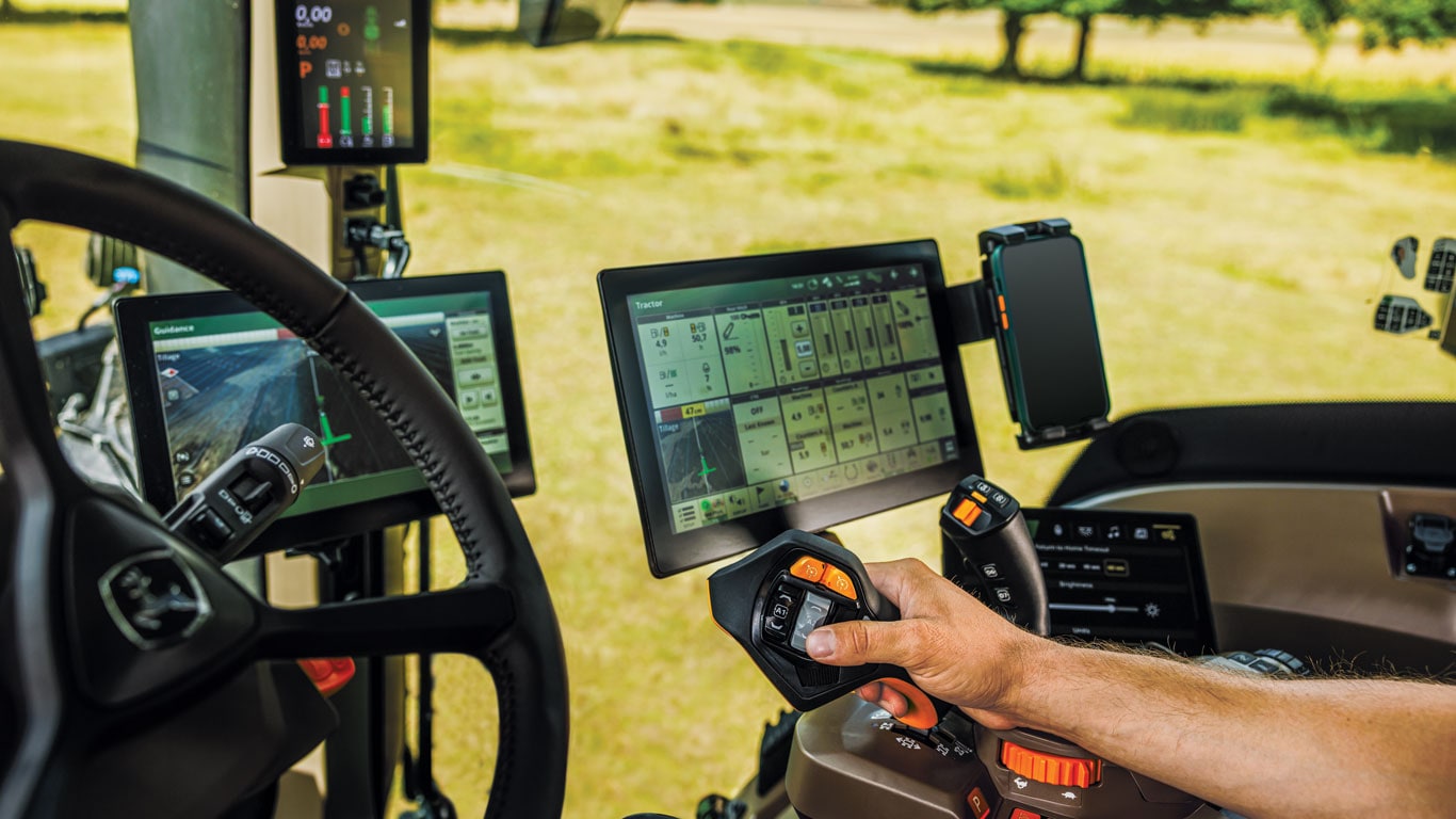 Gros plan de l’intérieur d’un tracteur 6R montrant les contrôleurs et les écrans d’affichage.