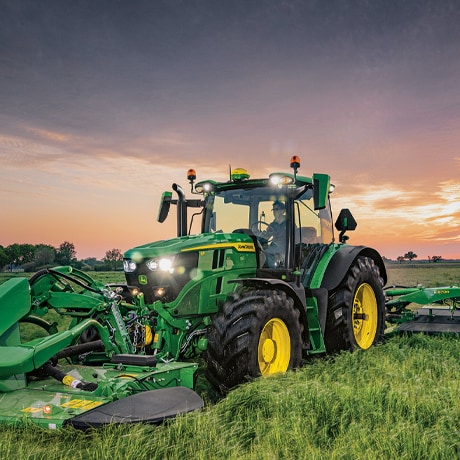 Tracteur tondant de l'herbe haute à la tombée du jour