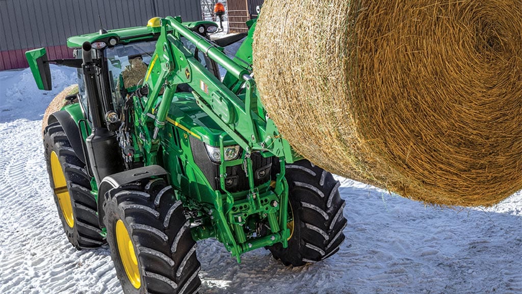 6r series tractor lifting hay bale with front loader