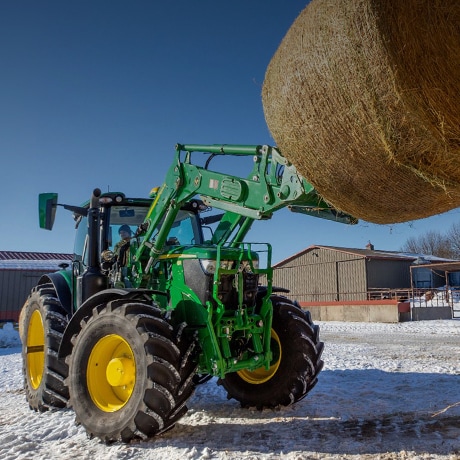 Tracteur soulevant une balle de foin ronde avec un chargeur frontal