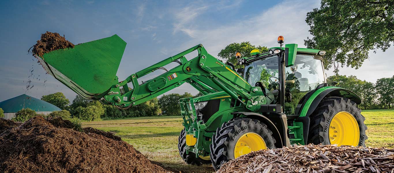 Tracteur 6r soulevant un tas de compost avec un chargeur frontal