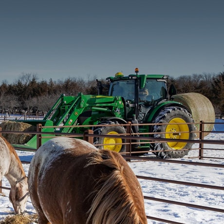 Tracteur sur une ferme et chevaux dans la neige