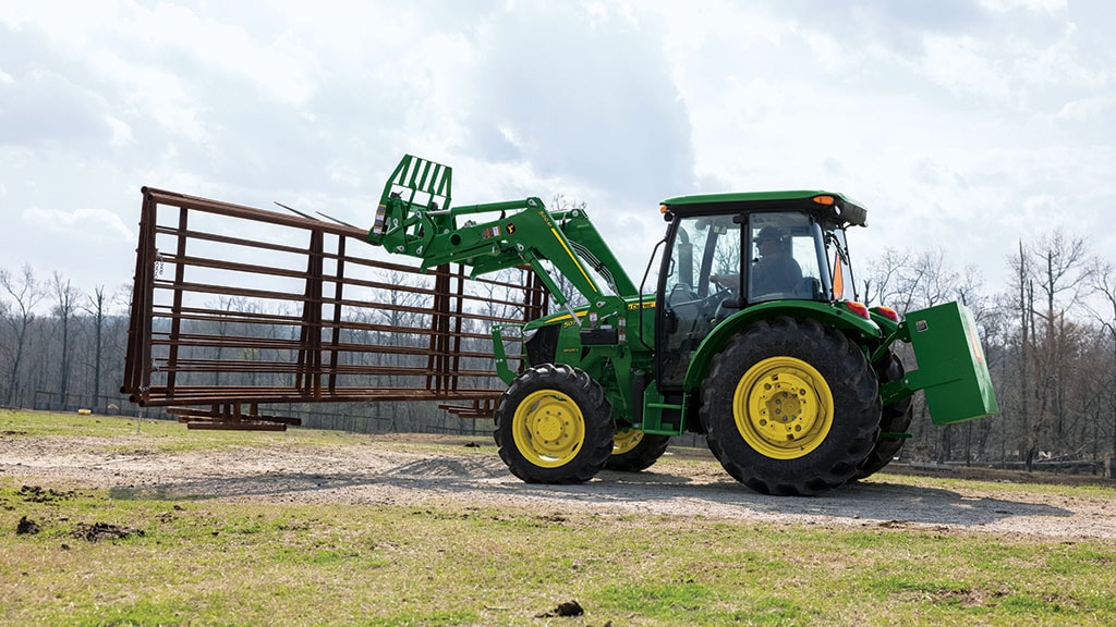 ​Un tracteur vert utilise une fourche à palette pour déplacer des planches sous une zone de stockage ouverte.