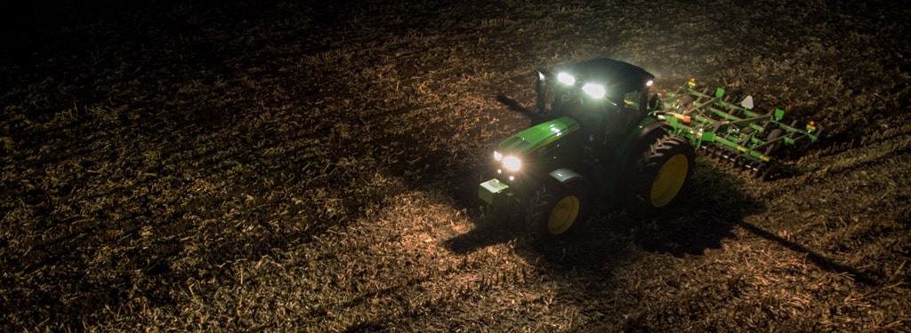 Image d'un tracteur pour culture en lignes dans un champ la nuit, phares allumés