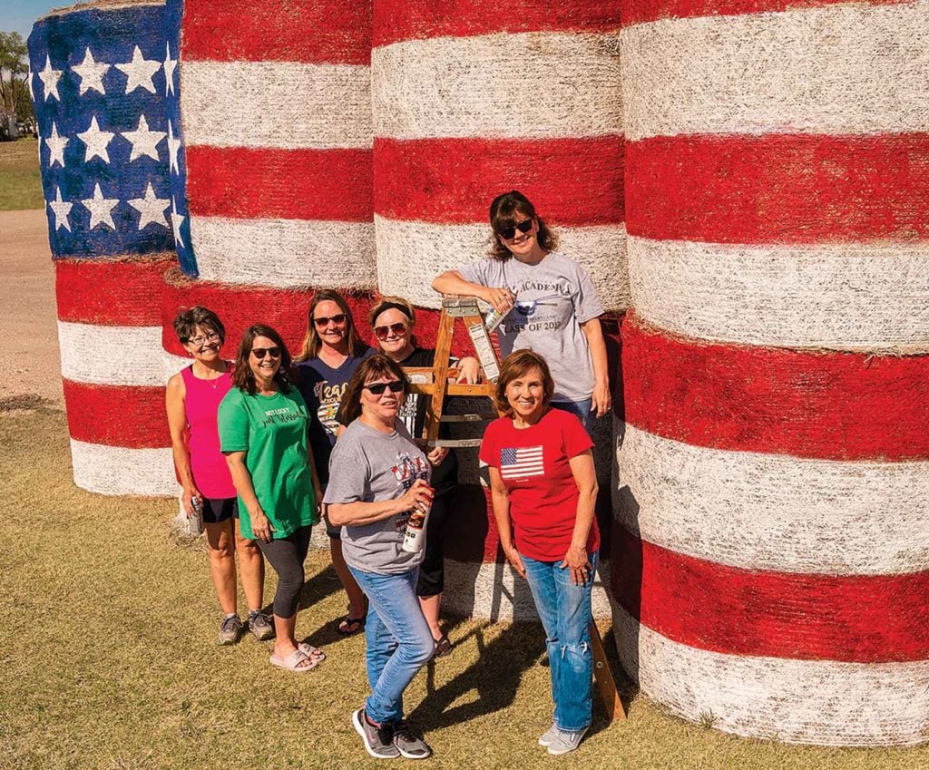 Women beside hay bales that are painted as flag