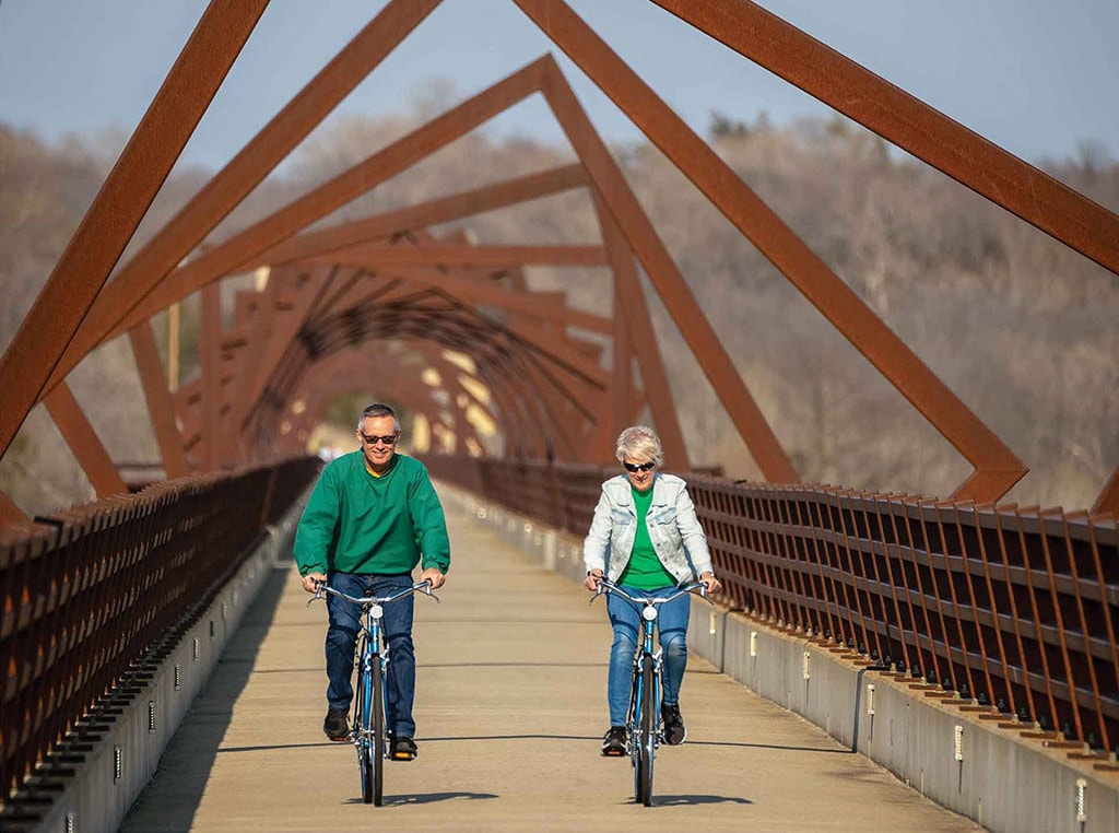 Homme et femme faisant une promenade à vélo sur un pont doté d’une structure décorative toute en angles