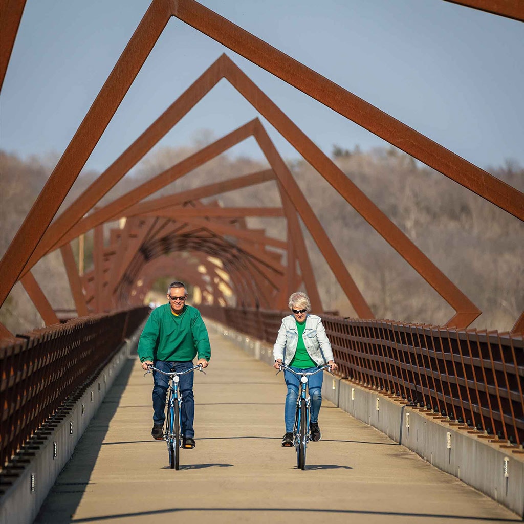 Homme et femme faisant une promenade à vélo sur un pont doté d’une structure décorative toute en angles