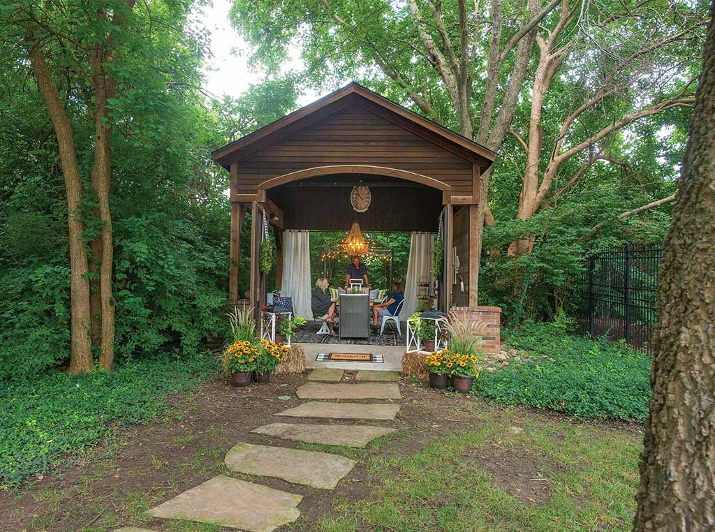 people in ornate open-air shed in yard with trees and flower pots