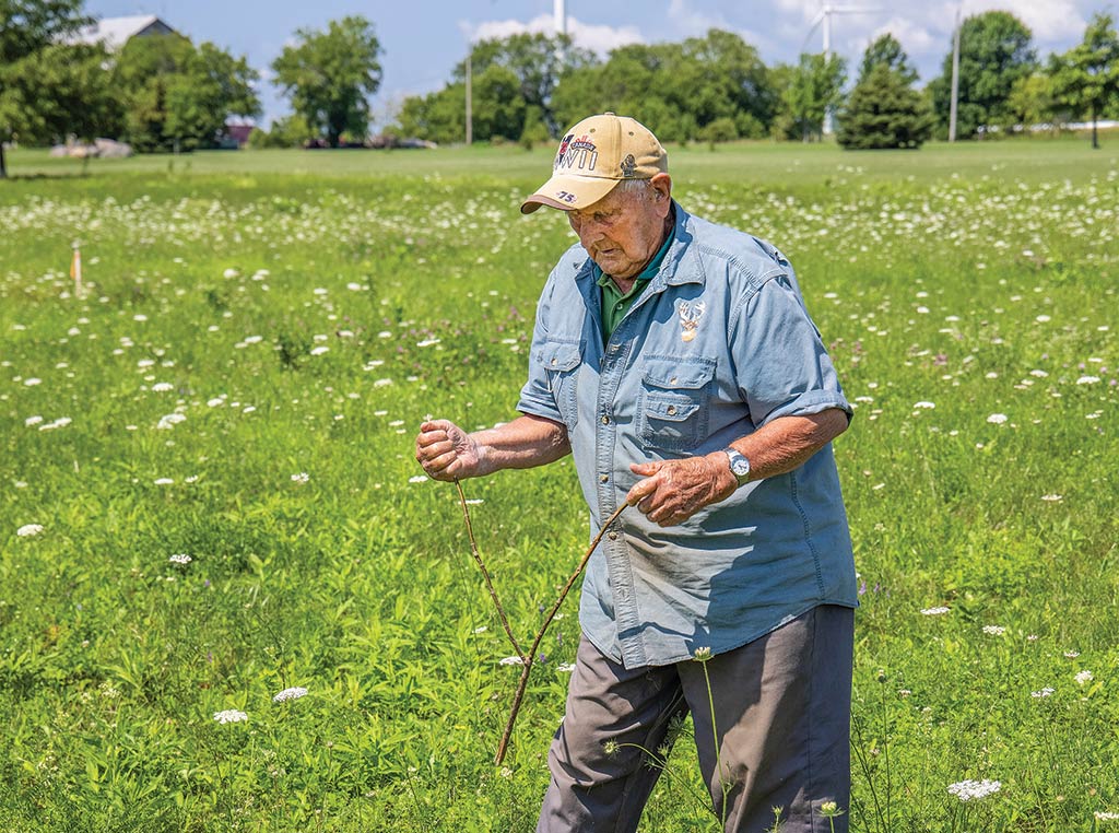 man in field with tree branch in his hand