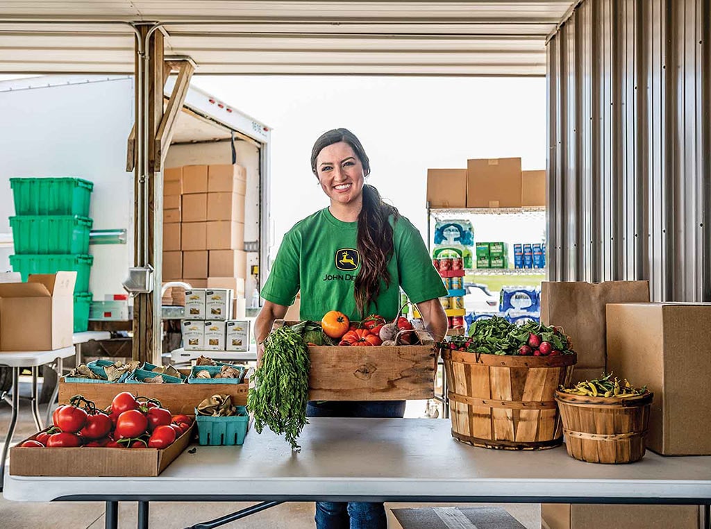 Employée de John Deere en train de mettre des cageots de fruits et légumes frais dans un camion