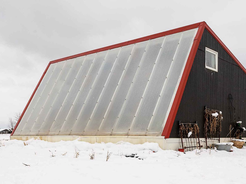 Serre de couleur noire avec bordures rouges et fenêtres blanches translucides entourée de neige