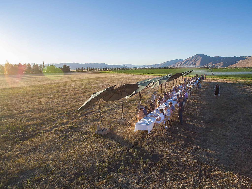 People sitting at white tablecloth dining tables in a field with mountains in the background