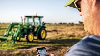 Homme dans un champ utilisant l’application John Deere Property Center avec un tracteur en arrière-plan