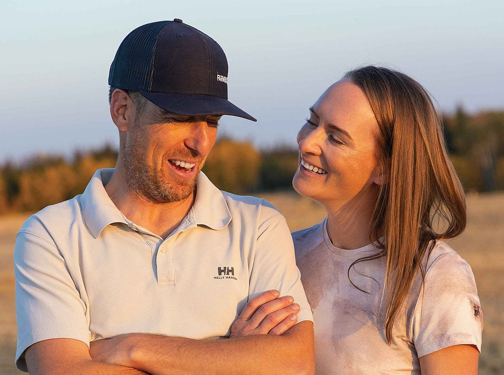 man with crossed arms smiling with woman in field