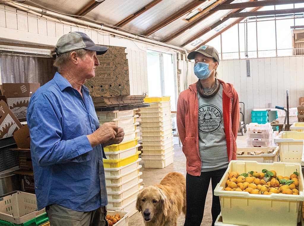 two people standing in front of crate of pears in farm warehouse