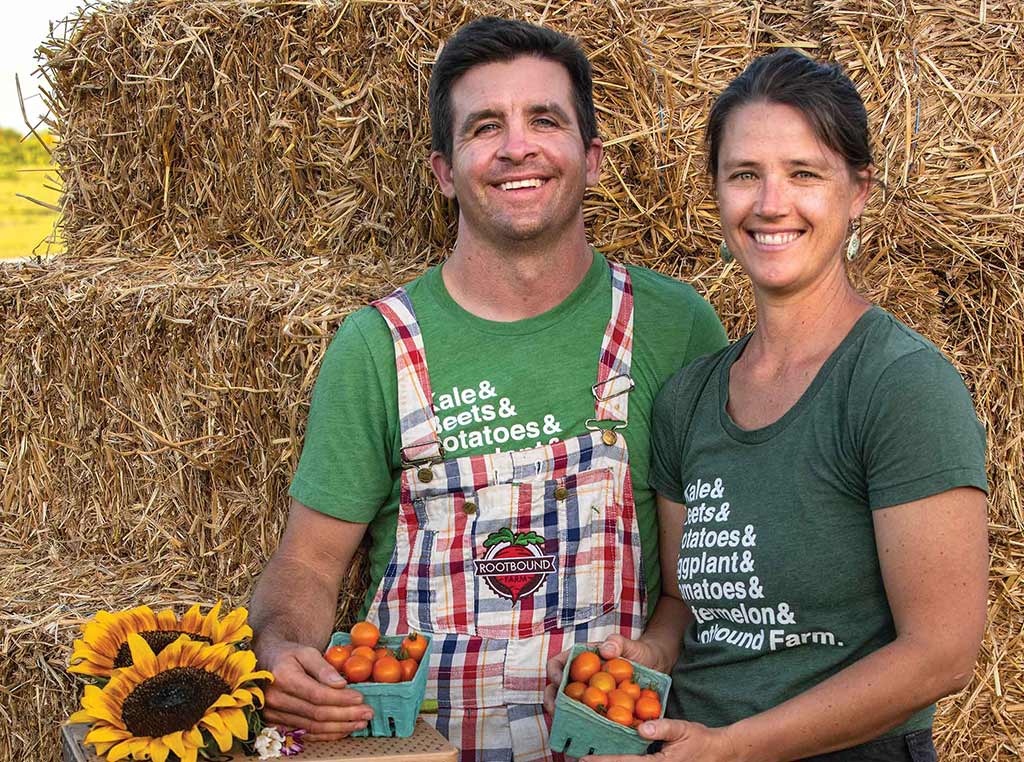 Homme et femme qui sourient en tenant des casseaux de tomates devant des balles de foin