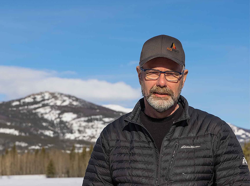 man with baseball cap and glasses with snowy hills in background