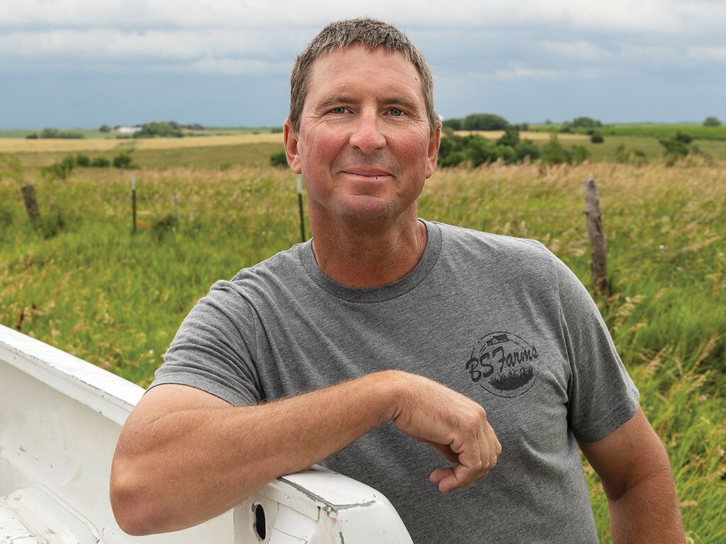 person grinning in field leaning on pickup truck with grey tshirt