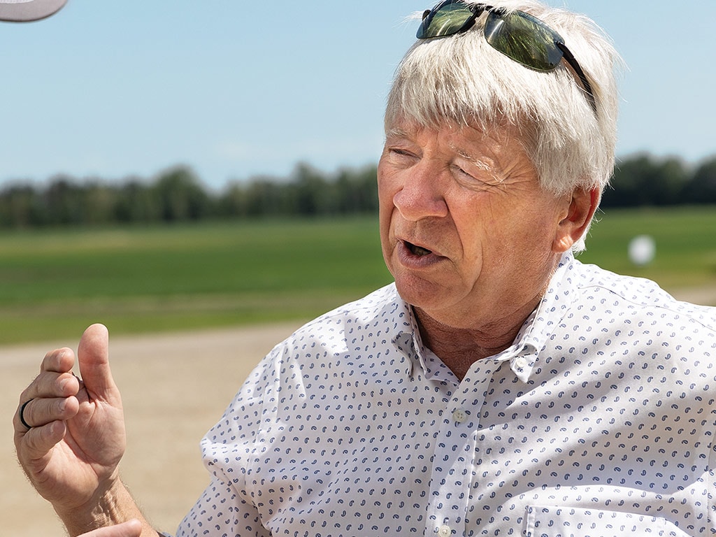 Personne qui gesticule en parlant, avec un champ et des arbres flous en arrière-plan