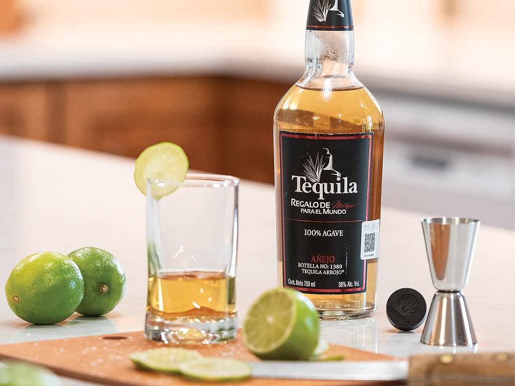 Bouteille de tequila añejo entourée d’un verre, d’un doseur et de limes