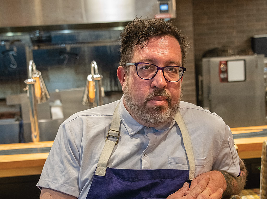 restaurant chef in apron with fingers interlocked and arm tattoos