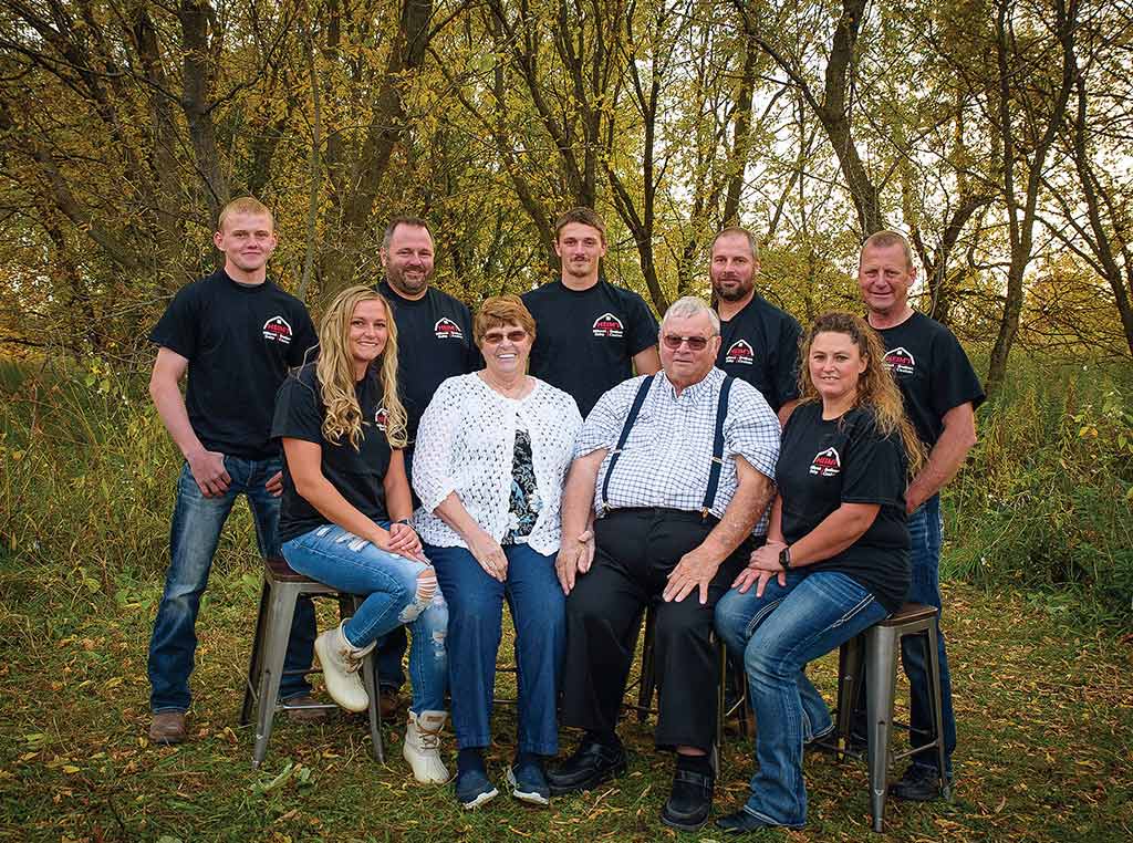 men and women standing and sitting with line of trees behind