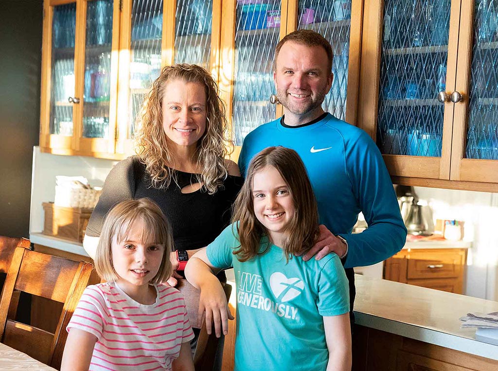 two parents and two daughters standing in kitchen smiling