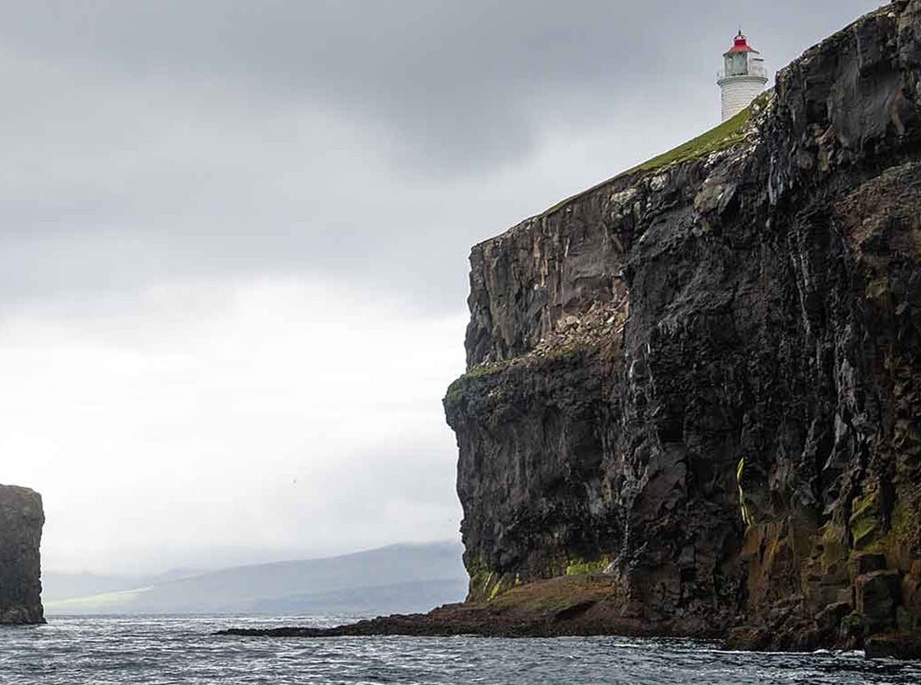 lighthouse on top of cliff surrounded by ocean