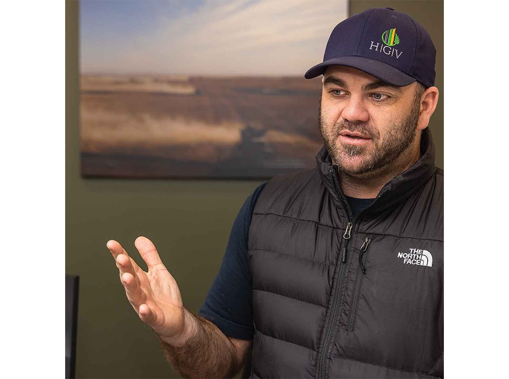 man with hand raised in a conversational gesture while wearing a north face vest and blue ball cap