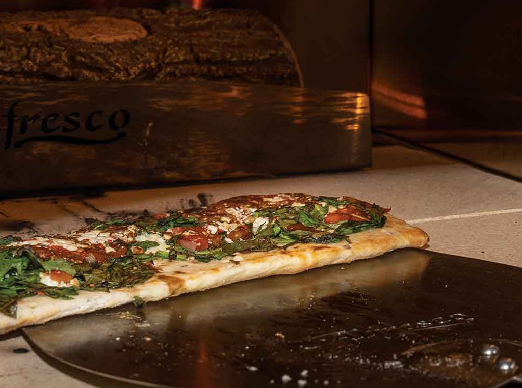 closeup of flatbread pizza being placed in wood burning oven