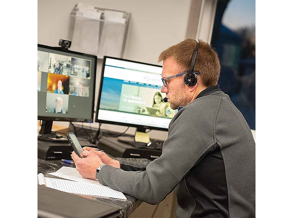 man with glasses sitting at desk with two computer monitors