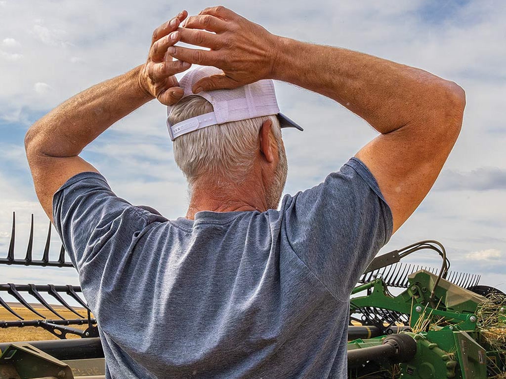 Personne vue de dos qui porte une casquette de baseball blanche et un t-shirt bleu et qui a les mains posées derrière sa tête devant de l’équipement John Deere