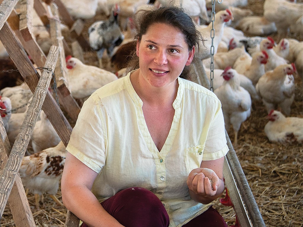 Une agricultrice, genou au sol, parmi des poules