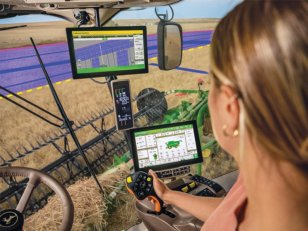 Vue par-dessus l’épaule d’une agricultrice dans la cabine d’une moissonneuse John Deere, sur le système d’automatisation de braquage AutoTrac