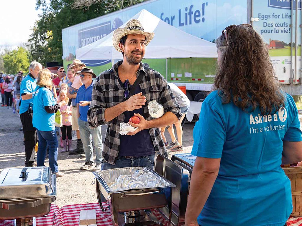 Person in straw hat standing at outdoor market stand smiling with worker